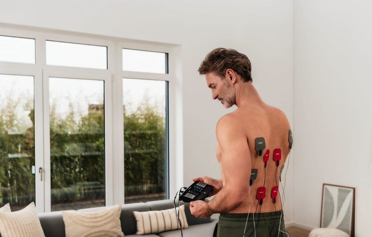 Man using the Beurer EM 89 TENS and EMS device on his back at home