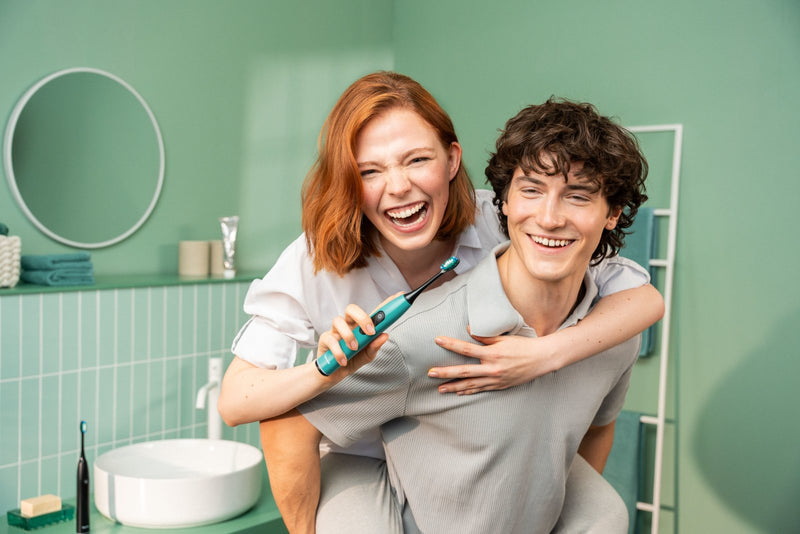 Two friends laughing in a bathroom, one brushing with the Beurer SC 50 Ocean Breeze sonic toothbrush
